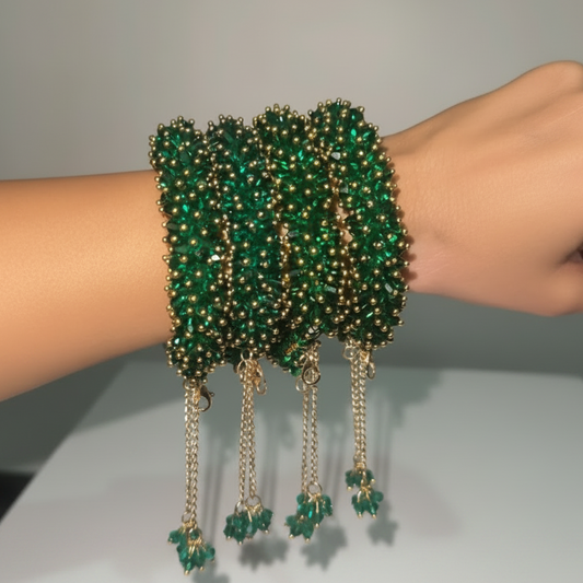 A close-up of a person's wrist wearing a stack of wide green beaded bracelets with gold-tone chain and bead detailing, set against a plain light gray background.