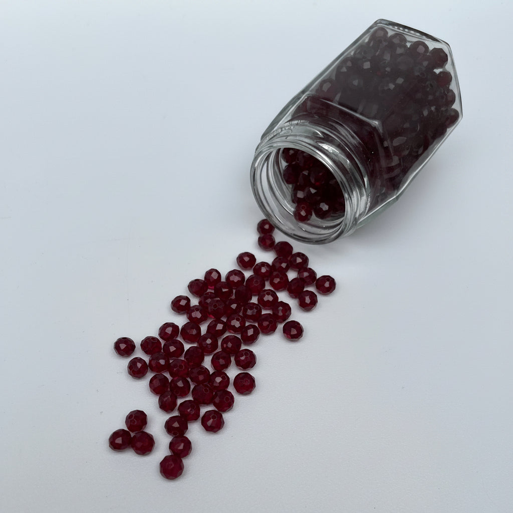 Glass jar with red beads spilling out on a white background