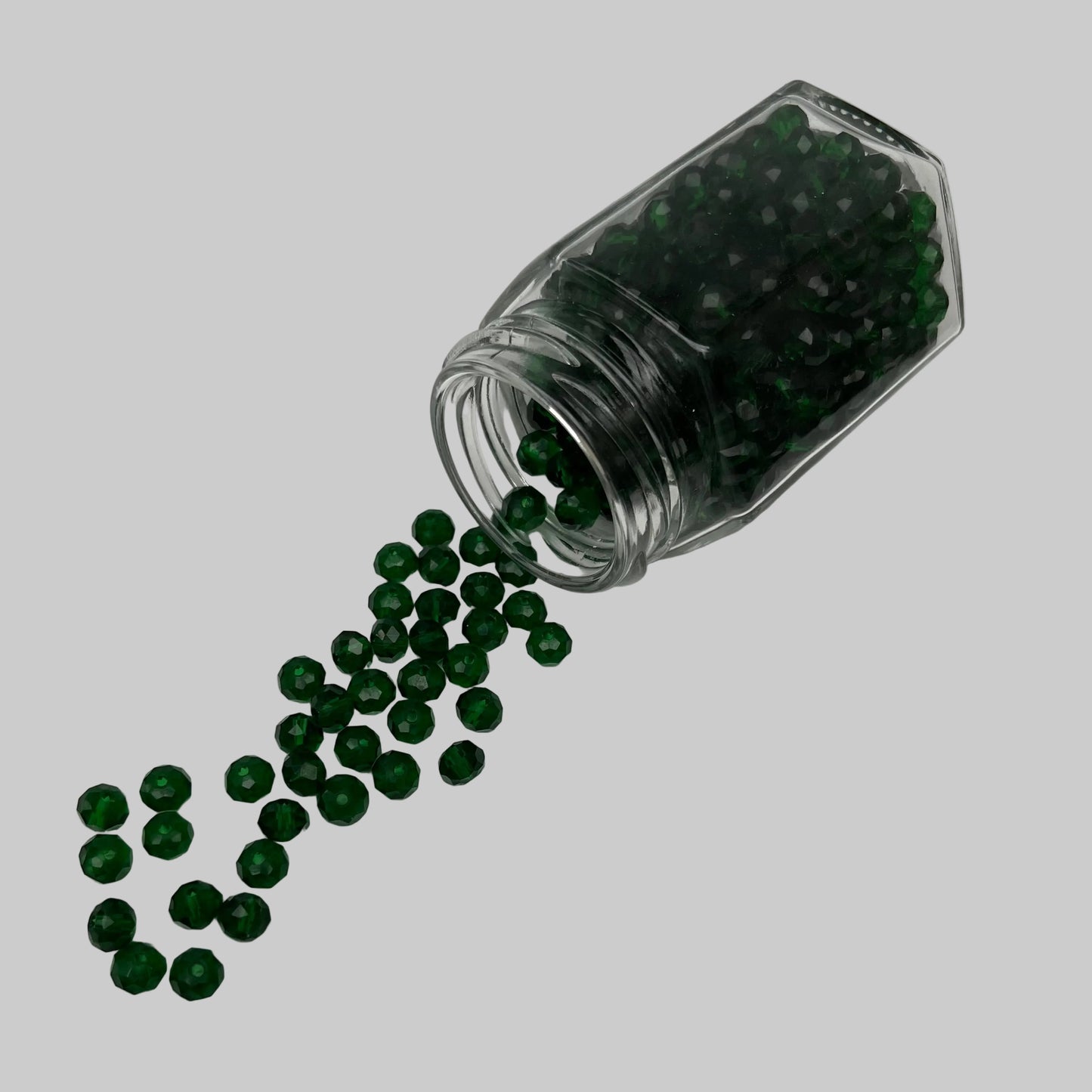Clear jar with green beads spilling out on a gray background
