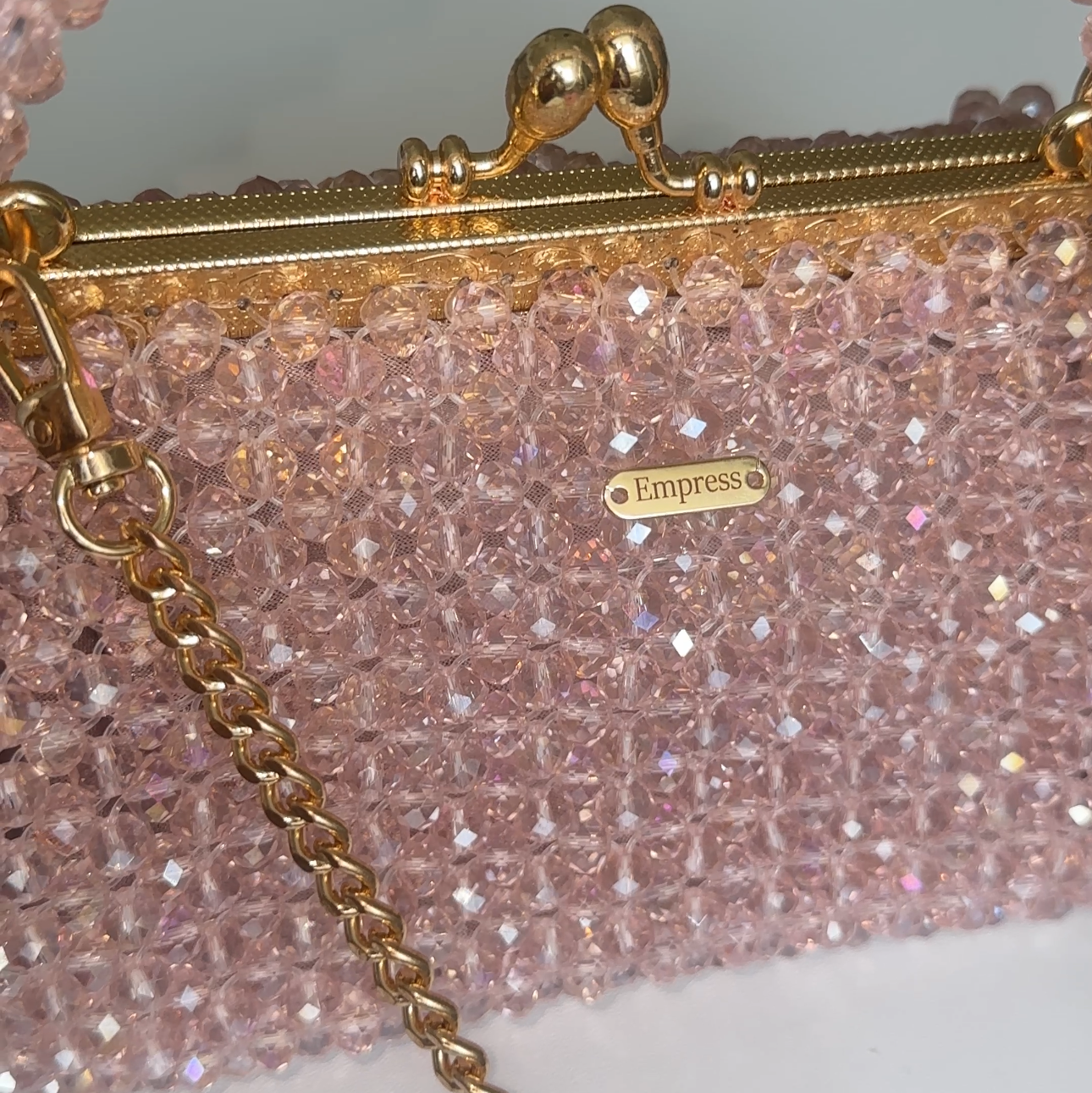 Pink glittery handbag with gold chain strap on a white background