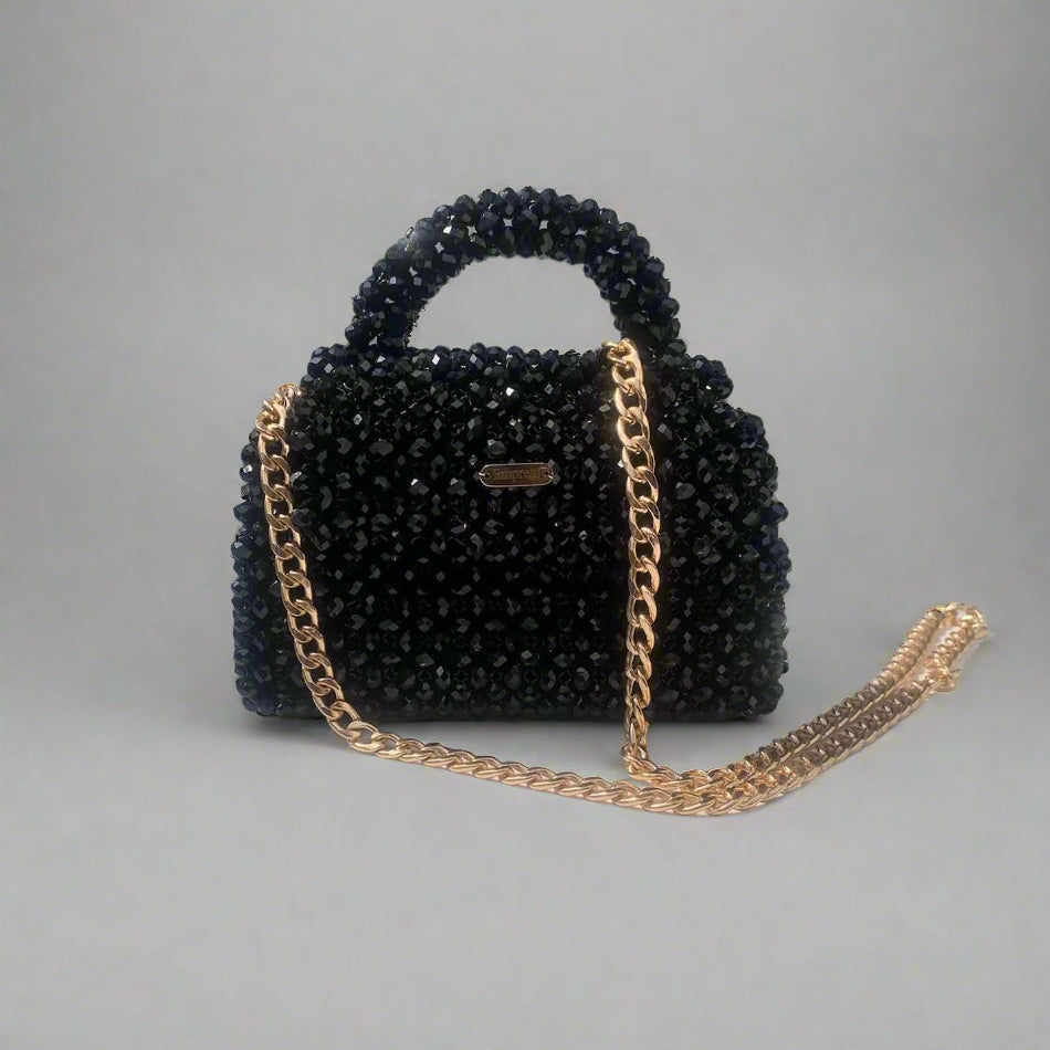 Black beaded handbag with gold chain strap on a gray background