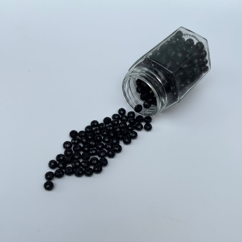 Small glass jar with black beads spilling out on a light gray background