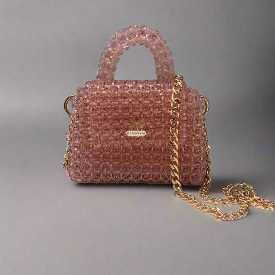 Pink beaded handbag with gold chain on a gray background
