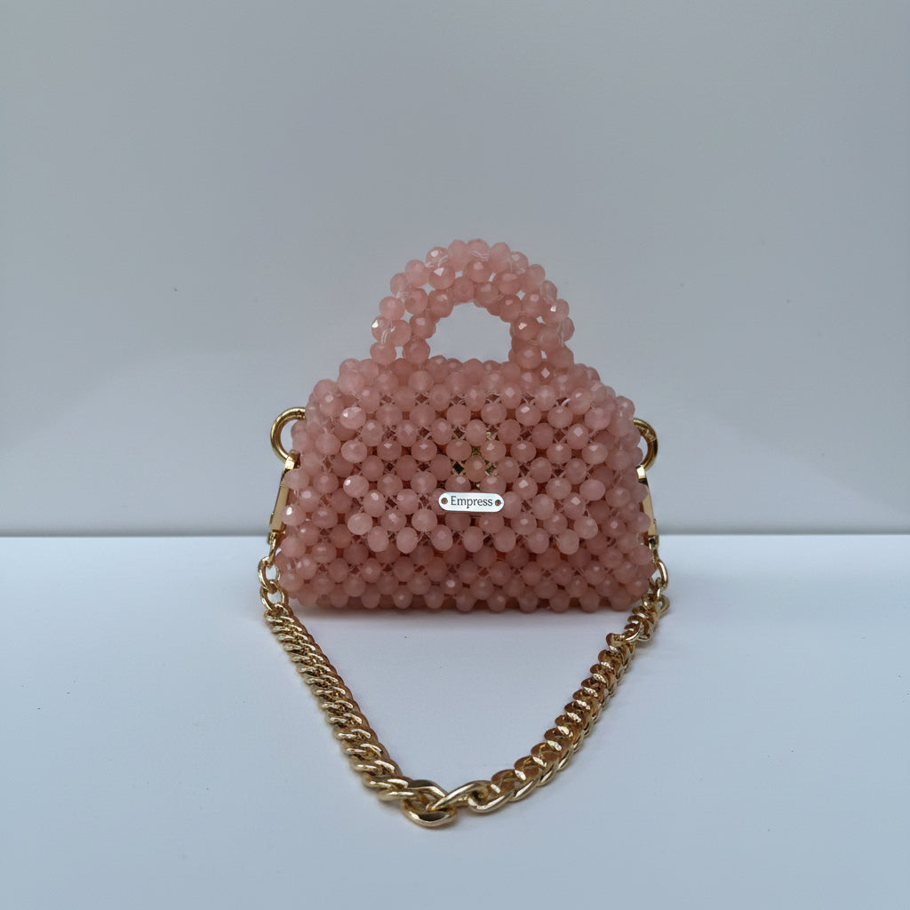 Pink beaded handbag with a gold chain strap on a white background