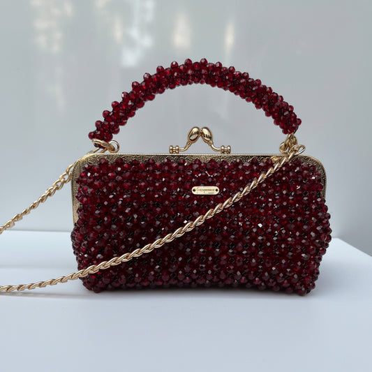 Burgundy beaded handbag with gold chain strap on a white surface